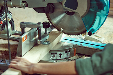 Image showing Busy and serious craftswoman grinding timbers with special machine.