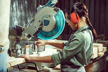 Image showing Busy and serious craftswoman grinding timbers with special machine.