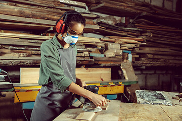 Image showing Busy and serious craftswoman grinding timbers with special machine.