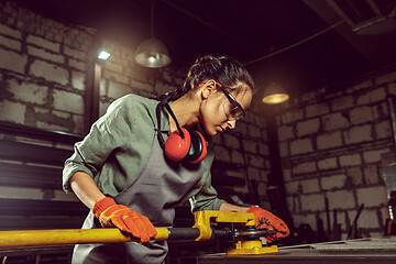 Image showing Busy and serious craftswoman grinding timbers with special machine.