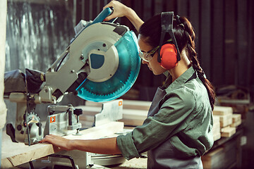 Image showing Busy and serious craftswoman grinding timbers with special machine.