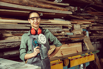 Image showing Smiling craftswoman grinding timbers with special machine.