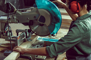 Image showing Busy and serious craftswoman grinding timbers with special machine.