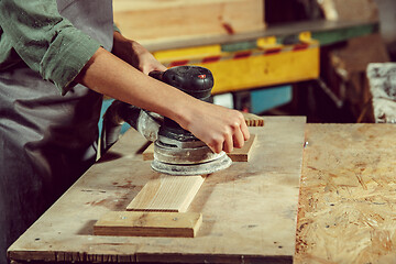 Image showing Hands of craftswoman grinding timbers with special machine.