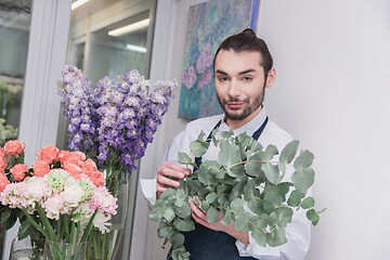 Image showing Small business. Male florist in flower shop. Floral design studio, making decorations and arrangements.