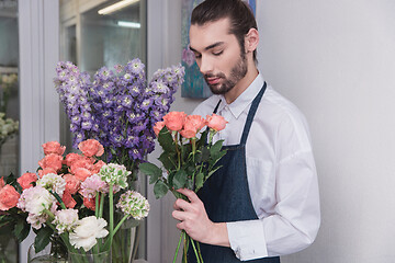 Image showing Small business. Male florist in flower shop. Floral design studio, making decorations and arrangements.