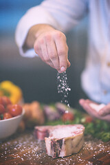 Image showing Chef putting salt on juicy slice of raw steak