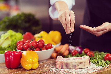 Image showing Chef putting salt on juicy slice of raw steak