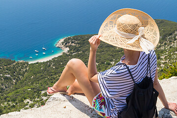 Image showing Active sporty woman on summer vacations sitting on old stone wall at Lubenice village, wearing straw hat and beach backpack enjoying beautiful coastal view of Cres island, Croatia