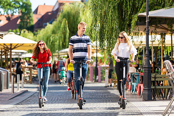 Image showing Trendy fashinable group of friends riding public rental electric scooters in urban city environment. New eco-friendly modern public city transport in Ljubljana, Slovenia