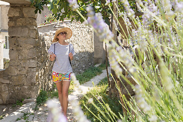 Image showing Beautiful blonde young female traveler wearing straw sun hat sightseeing and enjoying summer vacation in an old traditional village on Mediterranean cost