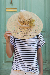 Image showing Unrecognizable female tourist woman wearing big straw standing in front of vinatage turquoise wooden door at old Mediterranean town