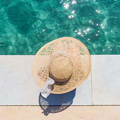 Image showing Woman wearing big summer sun hat relaxing on pier by clear turquoise sea.