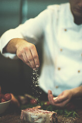 Image showing Chef putting salt on juicy slice of raw steak