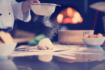 Image showing chef sprinkling flour over fresh pizza dough