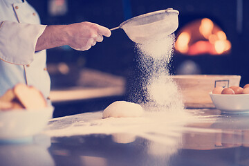 Image showing chef sprinkling flour over fresh pizza dough