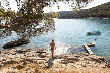 Image showing Young sporty man wearing red speedos tanning and realaxing on wild cove of Adriatic sea on a beach in shade of pine tree