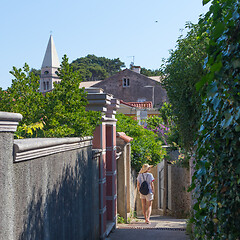 Image showing Rear view of beautiful blonde young female traveler wearing straw sun hat sightseeing and enjoying summer vacation in an old traditional costal town of Veli Losinj, Adriatic cost, Croatia