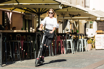 Image showing Trendy fashinable teenager girls riding public rental electric scooters in urban city environment. New eco-friendly modern public city transport in Ljubljana, Slovenia