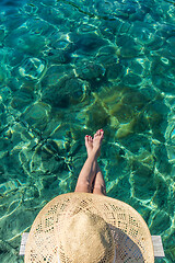 Image showing Graphic image of top down view of woman wearing big summer sun hat relaxing on small wooden pier by clear turquoise sea