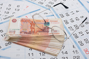 Image showing Glasses lie on a bundle of five-thousandth Russian banknotes, background from calendar sheets