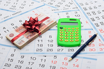 Image showing On the background from the calendar lies a bundle of money with a red bow, a calculator and a pen