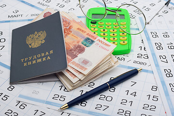 Image showing A bundle of five-thousandth bills sticks out of the work book, next to it lies a calculator and glasses and a pen