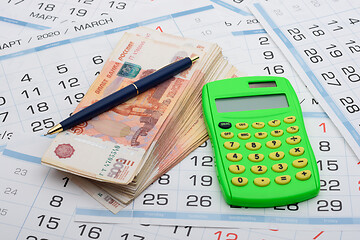 Image showing There is a wad of money on the calendar, a calculator and a pen