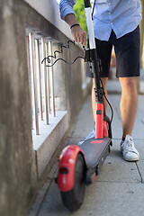 Image showing Male user safely parking electric scooter and locking it to a fence. Eco friendly green modern urban mobility concept of sharing transportation with electric scooters for rent in Ljubljana, Slovenia