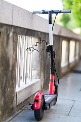 Image showing Red electric scooter parked and safely chained to a fence. Eco friendly green modern urban mobility concept of sharing transportation with electric scooters for rent in Ljubljana, Slovenia