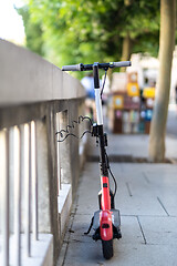 Image showing Red electric scooter parked and safely chained to a fence. Eco friendly green modern urban mobility concept of sharing transportation with electric scooters for rent in Ljubljana, Slovenia