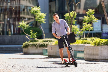 Image showing Young casual active sporty businessman in urban city center, wearing shirt and shorts, holding laptop bag, riding to work on electric scooter on a hot summer day