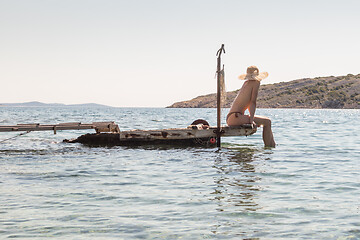 Image showing View of unrecognizable woman wearing big summer sun hat tanning topless and relaxing on old wooden pier in remote calm cove of Adriatic sea, Croatia