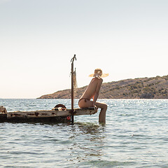 Image showing View of unrecognizable woman wearing big summer sun hat tanning topless and relaxing on old wooden pier in remote calm cove of Adriatic sea, Croatia