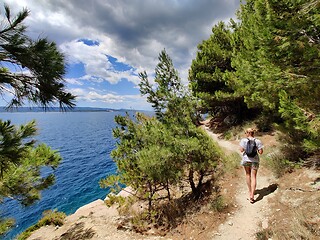 Image showing Young active feamle tourist wearing small backpack walking on coastal path among pine trees looking for remote cove to swim alone in peace on seaside in Croatia. Travel and adventure concept