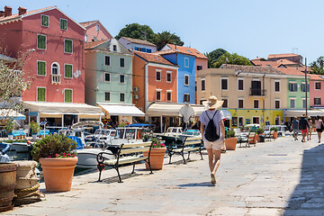 Image showing Rear view of beautiful blonde young female traveler wearing straw sun hat sightseeing and enjoying summer vacation in an old traditional costal town of Veli Losinj, Adriatic cost, Croatia