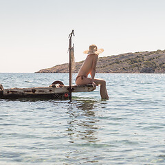 Image showing View of unrecognizable woman wearing big summer sun hat tanning topless and relaxing on old wooden pier in remote calm cove of Adriatic sea, Croatia