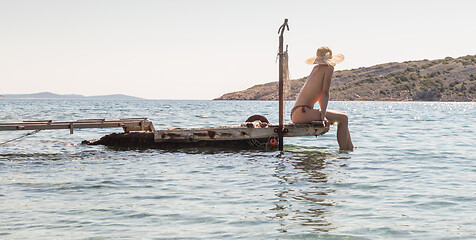 Image showing View of unrecognizable woman wearing big summer sun hat tanning topless and relaxing on old wooden pier in remote calm cove of Adriatic sea, Croatia