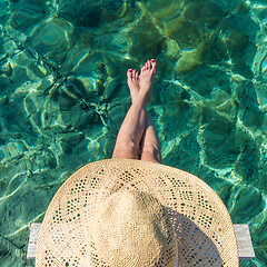 Image showing Graphic image of top down view of woman wearing big summer sun hat relaxing on small wooden pier by clear turquoise sea