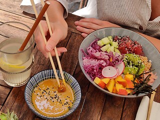 Image showing Woman eating tasty colorful healthy natural organic vegetarian Hawaiian poke bowl using asian chopsticks on rustic wooden table. Healthy natural organic eating concept