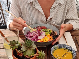Image showing Woman eating tasty colorful healthy natural organic vegetarian Hawaiian poke bowl using asian chopsticks on rustic wooden table. Healthy natural organic eating concept