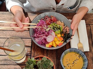 Image showing Woman eating tasty colorful healthy natural organic vegetarian Hawaiian poke bowl using asian chopsticks on rustic wooden table. Healthy natural organic eating concept