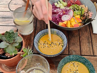 Image showing Woman eating tasty colorful healthy natural organic vegetarian Hawaiian poke bowl using asian chopsticks on rustic wooden table. Healthy natural organic eating concept