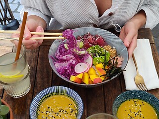 Image showing Woman eating tasty colorful healthy natural organic vegetarian Hawaiian poke bowl using asian chopsticks on rustic wooden table. Healthy natural organic eating concept