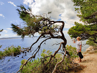 Image showing Young active feamle tourist taking a break, drinking water, wearing small backpack while walking on coastal path among pine trees looking for remote cove to swim alone in peace on seaside in Croatia