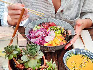 Image showing Woman eating tasty colorful healthy natural organic vegetarian Hawaiian poke bowl using asian chopsticks on rustic wooden table. Healthy natural organic eating concept