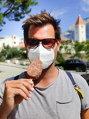 Image showing Young guy on summer vacations wearing corona virus protective face mask not beeing able to lick ice cream bar