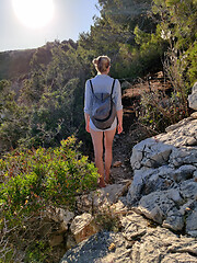 Image showing Young active feamle tourist wearing small backpack walking on coastal path among pine trees looking for remote cove to swim alone in peace on seaside in Croatia. Travel and adventure concept