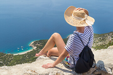 Image showing Active sporty woman on summer vacations sitting on old stone wall at Lubenice village, wearing straw hat and beach backpack enjoying beautiful coastal view of Cres island, Croatia