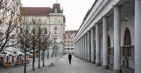 Image showing Rear view of unrecognizable woman walking in empty old medieval Ljubljana city center during corona virus pandemic. Almost no people outside on streets